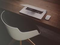 modern white chair in front of wood desk with laptop and mouse