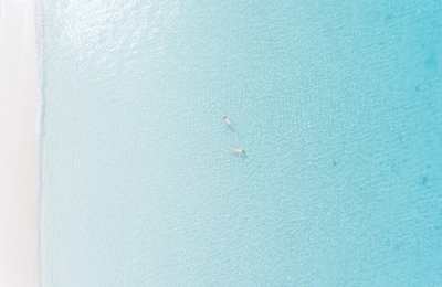 bird's view of white sand beach and turquoise water and two people swimming